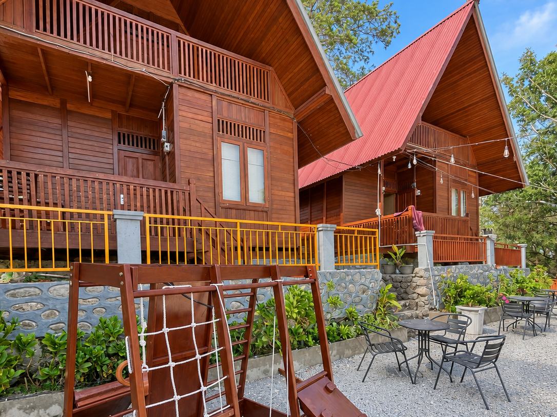 Villa Rumah Kayu, a two-storey wooden house with a balcony and a children's climbing frame in front, at D'Pines Peak Villa Malino